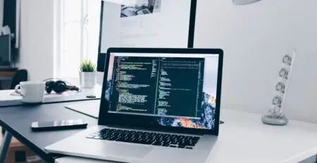 Mostrando um notebook em uma mesa branca com um código de programador na tela.